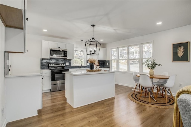 kitchen featuring pendant lighting, a center island, white cabinets, light hardwood / wood-style floors, and stainless steel appliances