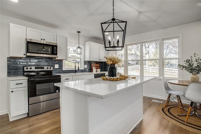 kitchen featuring a kitchen island, stainless steel appliances, white cabinetry, and a healthy amount of sunlight