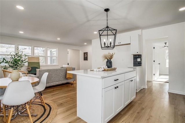 kitchen with pendant lighting, a center island, ceiling fan with notable chandelier, light hardwood / wood-style floors, and white cabinetry