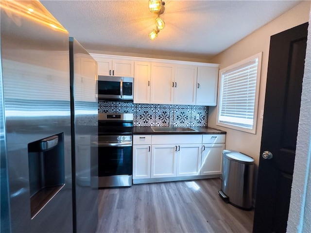 kitchen featuring appliances with stainless steel finishes, sink, white cabinets, decorative backsplash, and light hardwood / wood-style flooring