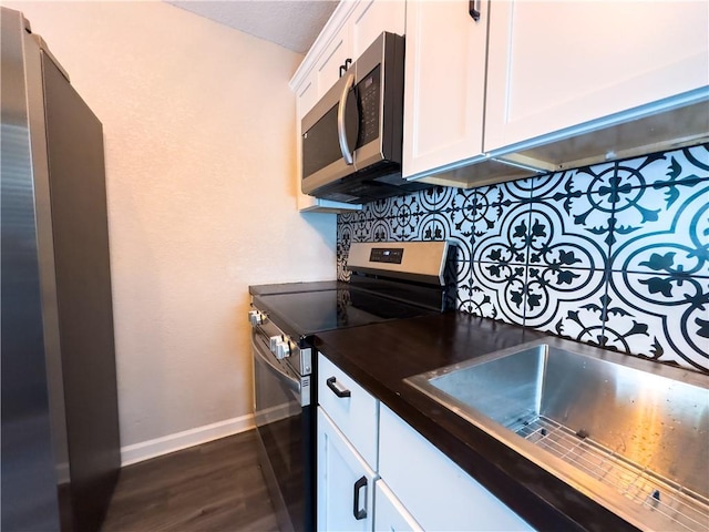 kitchen with sink, white cabinets, dark hardwood / wood-style flooring, appliances with stainless steel finishes, and tasteful backsplash