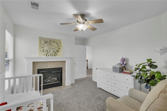 interior space with a tiled fireplace, light colored carpet, and ceiling fan