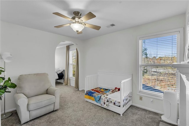 carpeted bedroom featuring ceiling fan and a nursery area