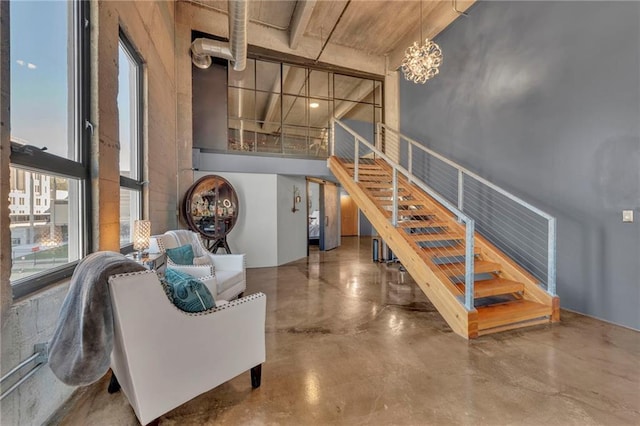 staircase featuring a notable chandelier, a towering ceiling, and concrete floors