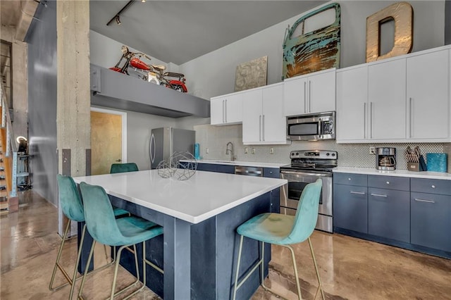 kitchen with white cabinetry, backsplash, a breakfast bar area, a kitchen island, and appliances with stainless steel finishes