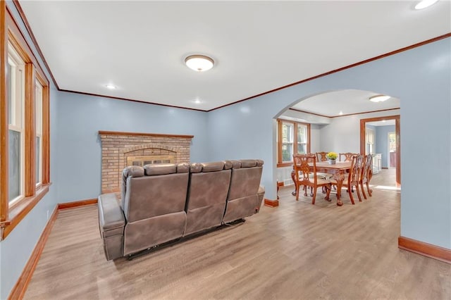 living room featuring light hardwood / wood-style floors, crown molding, and a brick fireplace