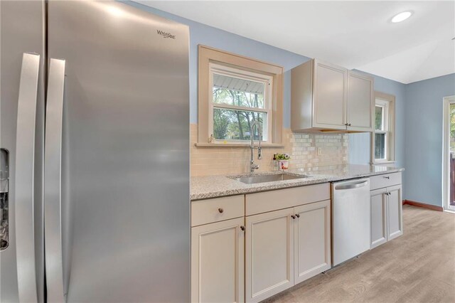 kitchen featuring light stone countertops, appliances with stainless steel finishes, sink, light hardwood / wood-style floors, and decorative backsplash