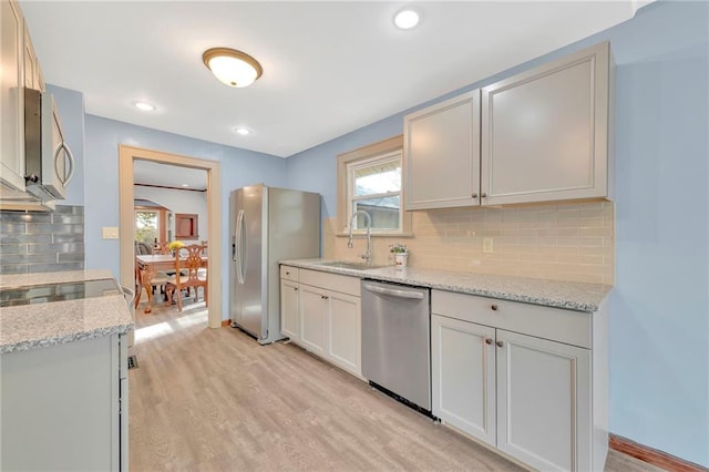 kitchen featuring tasteful backsplash, light stone counters, appliances with stainless steel finishes, light hardwood / wood-style flooring, and sink