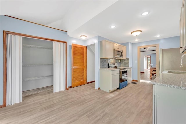 kitchen featuring tasteful backsplash, appliances with stainless steel finishes, light stone countertops, light wood-type flooring, and sink