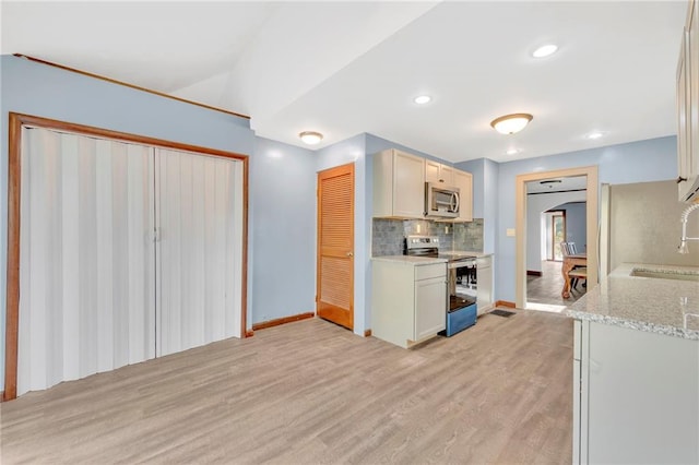 kitchen featuring decorative backsplash, white cabinets, appliances with stainless steel finishes, light hardwood / wood-style flooring, and light stone counters