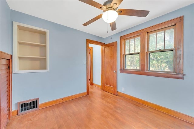 empty room featuring ceiling fan, light hardwood / wood-style flooring, and built in shelves