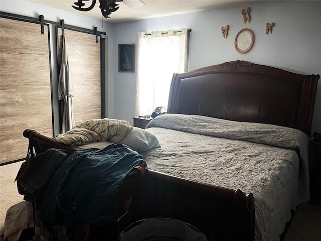 carpeted bedroom with wood walls, a barn door, and ceiling fan