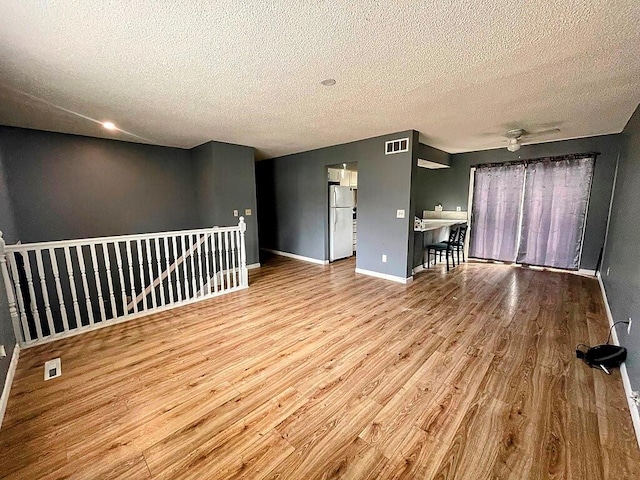 unfurnished living room featuring light hardwood / wood-style flooring, a textured ceiling, and ceiling fan