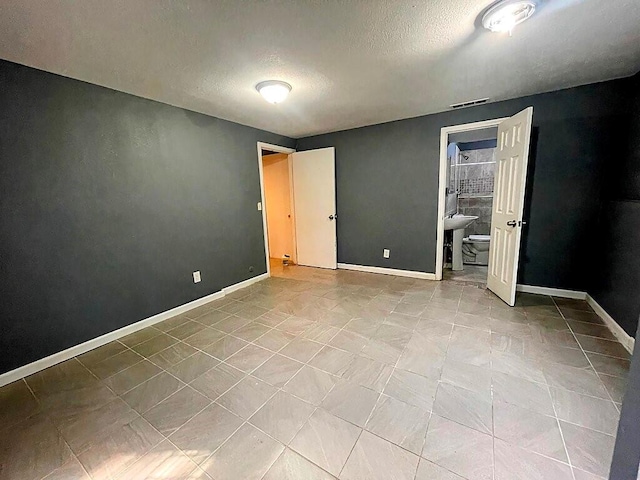 unfurnished bedroom featuring a textured ceiling, ensuite bath, and light tile patterned floors