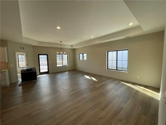 unfurnished living room featuring a chandelier, dark hardwood / wood-style flooring, and a tray ceiling