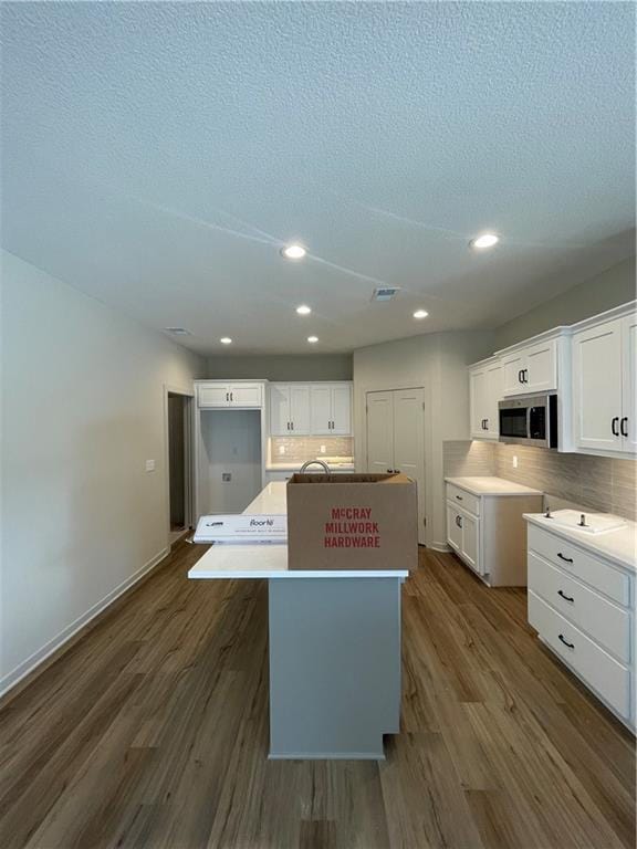 kitchen featuring white cabinetry, dark hardwood / wood-style floors, a center island with sink, and a textured ceiling