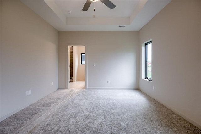 carpeted spare room with a raised ceiling, a ceiling fan, and visible vents