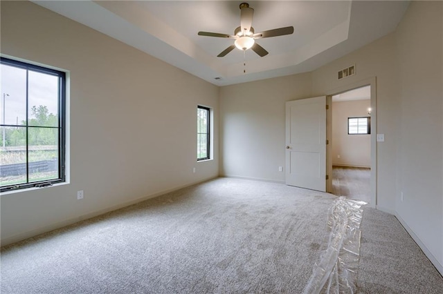 spare room featuring light carpet, a raised ceiling, a ceiling fan, baseboards, and visible vents