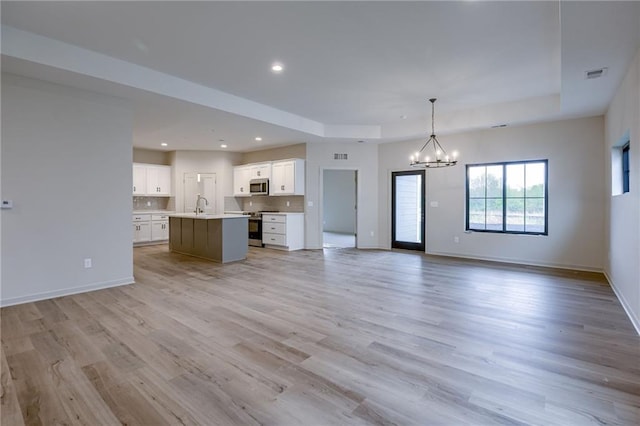 unfurnished living room featuring light wood-style floors, visible vents, a raised ceiling, baseboards, and an inviting chandelier