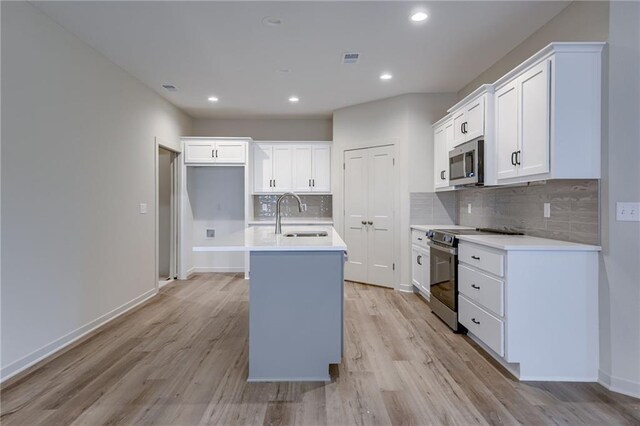 kitchen featuring a kitchen island with sink, light wood-type flooring, tasteful backsplash, a sink, and appliances with stainless steel finishes