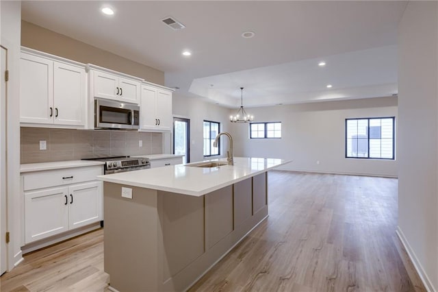 kitchen with a sink, light countertops, light wood finished floors, stainless steel appliances, and an island with sink