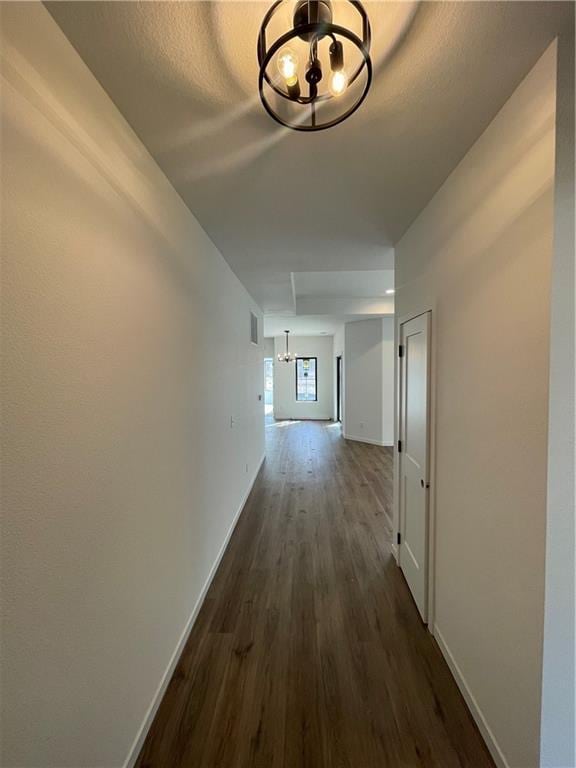 corridor featuring visible vents, baseboards, an inviting chandelier, and dark wood-style flooring