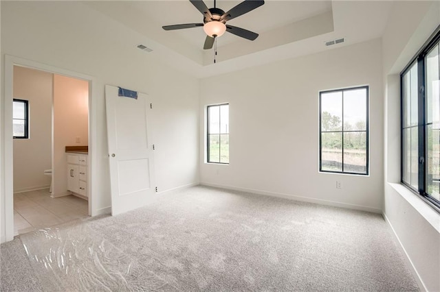 unfurnished bedroom with light colored carpet, a tray ceiling, visible vents, and baseboards