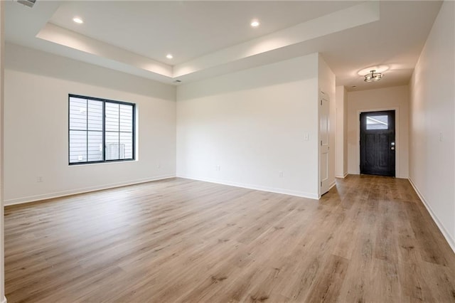spare room featuring recessed lighting, baseboards, light wood-style flooring, and a tray ceiling