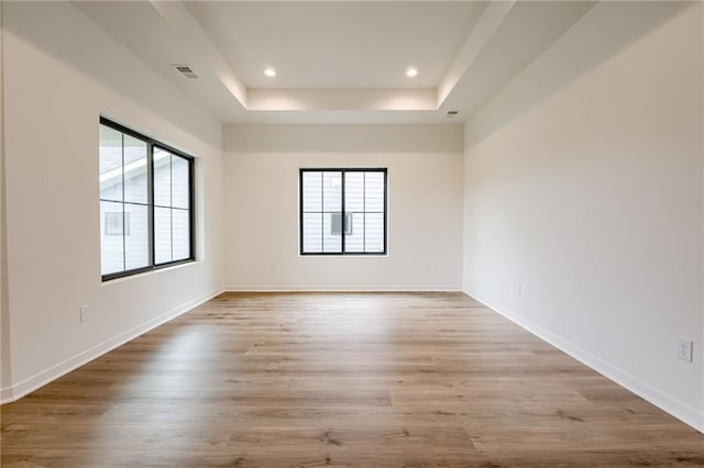 empty room with a tray ceiling, plenty of natural light, baseboards, and light wood-type flooring