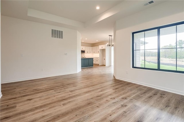 unfurnished living room with a chandelier, baseboards, visible vents, and light wood-style floors