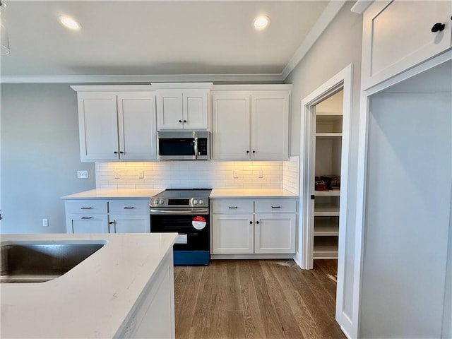 kitchen with tasteful backsplash, appliances with stainless steel finishes, wood-type flooring, and white cabinets