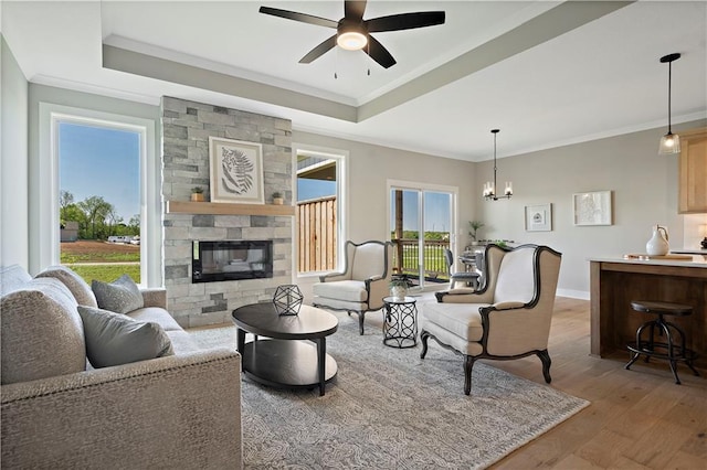 living room featuring crown molding, a tray ceiling, a stone fireplace, and hardwood / wood-style floors