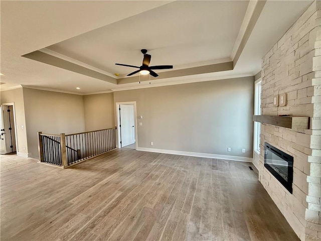 unfurnished living room with crown molding, hardwood / wood-style flooring, a stone fireplace, and a raised ceiling