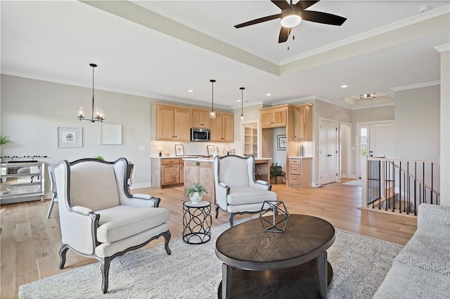 living room with a tray ceiling, crown molding, ceiling fan with notable chandelier, and light wood-type flooring