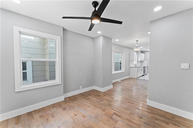 unfurnished living room with sink, light wood-type flooring, and ceiling fan with notable chandelier