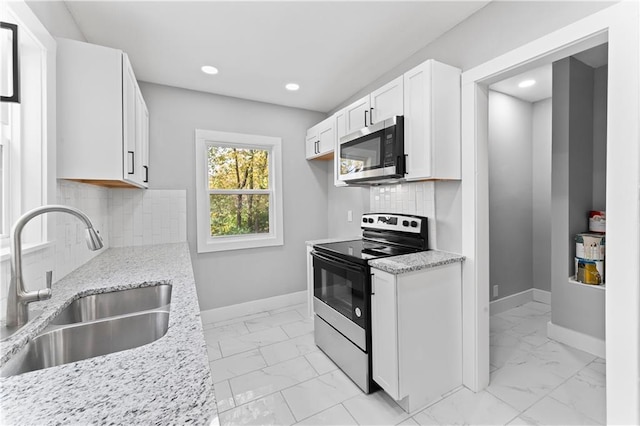 kitchen with white cabinets, tasteful backsplash, appliances with stainless steel finishes, light stone countertops, and sink