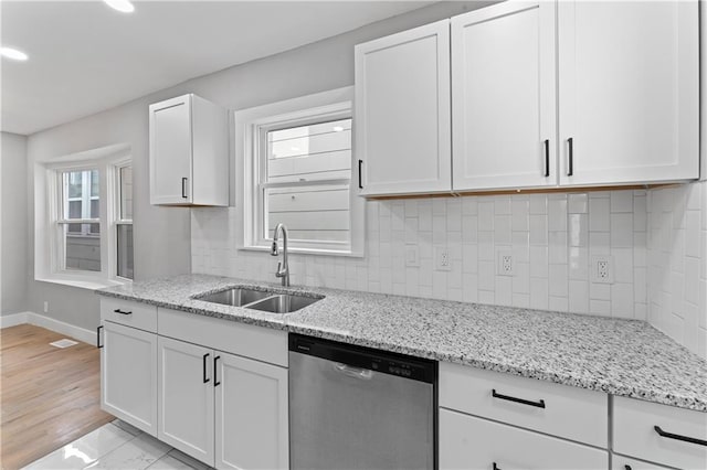 kitchen featuring stainless steel dishwasher, sink, white cabinetry, and light stone countertops