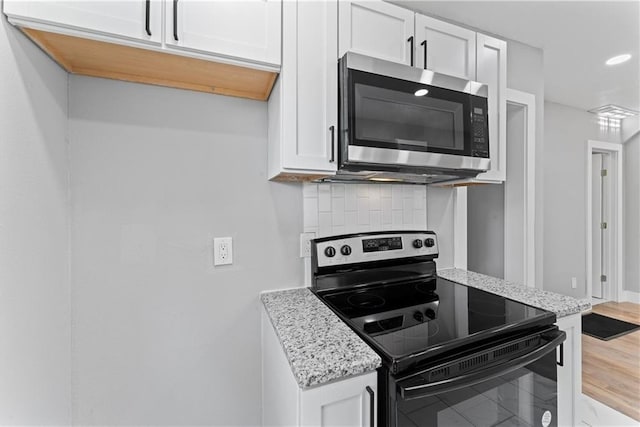 kitchen featuring decorative backsplash, wood-type flooring, light stone countertops, black / electric stove, and white cabinetry