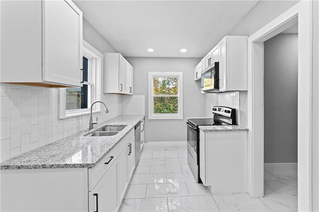 kitchen with decorative backsplash, white cabinets, light stone counters, appliances with stainless steel finishes, and sink