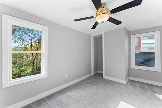 unfurnished bedroom featuring multiple windows, light colored carpet, and ceiling fan