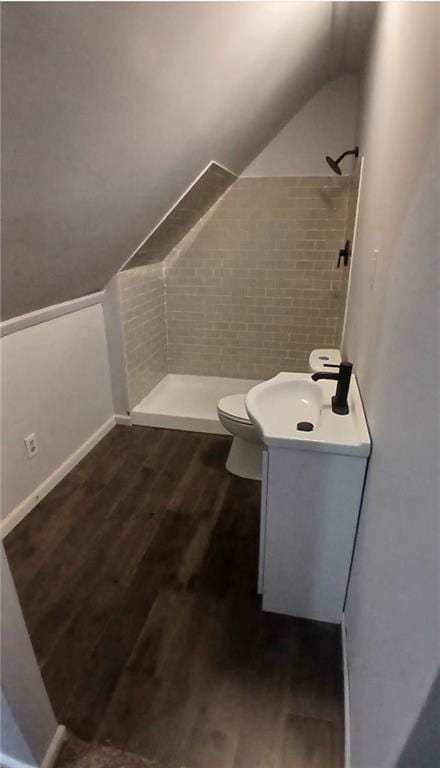 full bathroom with vanity, vaulted ceiling, toilet, tiled shower, and wood finished floors