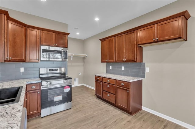 kitchen featuring decorative backsplash, light stone countertops, stainless steel appliances, and light hardwood / wood-style flooring