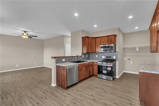 kitchen with kitchen peninsula, appliances with stainless steel finishes, ceiling fan, sink, and light hardwood / wood-style flooring