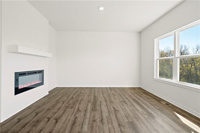 unfurnished living room featuring heating unit, a healthy amount of sunlight, and wood-type flooring