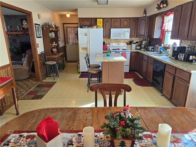 kitchen with tasteful backsplash, a kitchen island, sink, white appliances, and a breakfast bar area