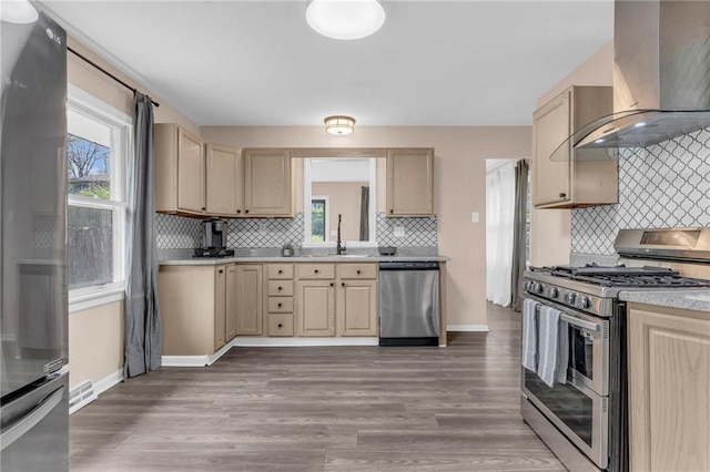 kitchen featuring tasteful backsplash, wall chimney range hood, appliances with stainless steel finishes, and a healthy amount of sunlight