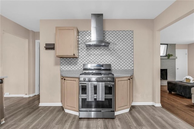 kitchen with range with two ovens, light brown cabinetry, wall chimney range hood, and dark hardwood / wood-style floors