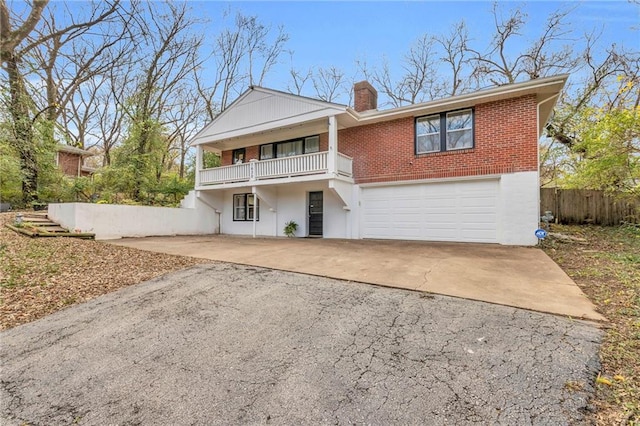 view of front facade featuring a garage, a balcony, a chimney, aphalt driveway, and brick siding