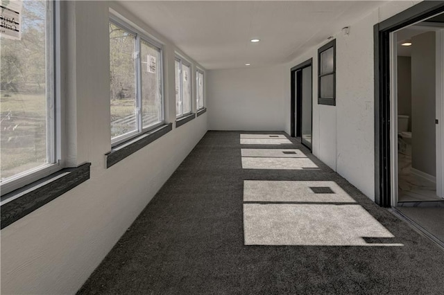 hall featuring plenty of natural light and dark colored carpet