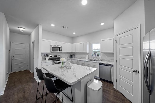 kitchen featuring a kitchen island, dark hardwood / wood-style floors, a breakfast bar area, white cabinetry, and appliances with stainless steel finishes